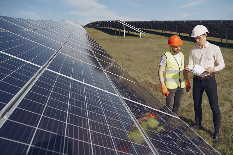 Engenheiro e funcionário conversando em frente a placas de energia solar